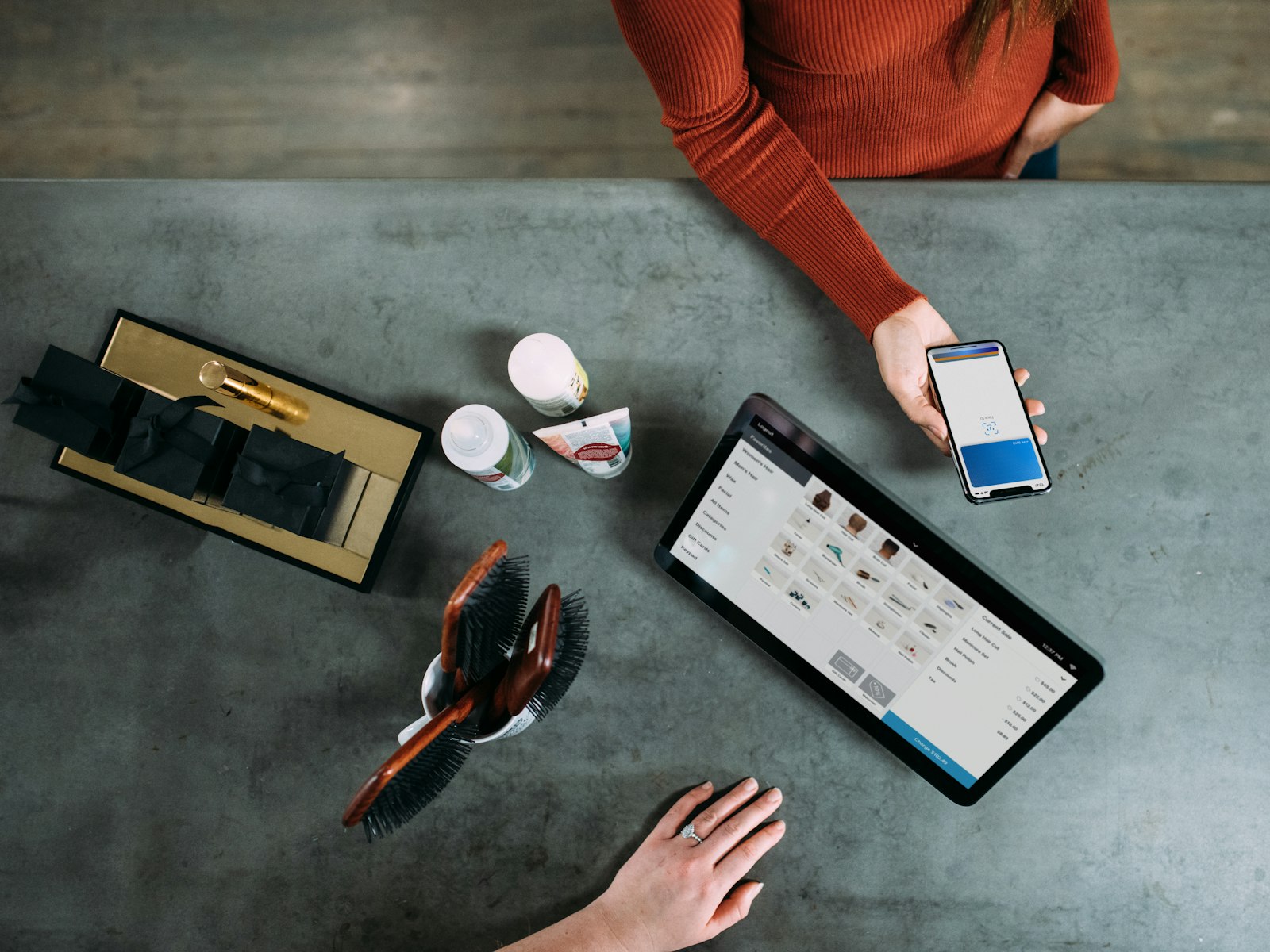 Overhead view of a customer paying by smartphone at a shop counter beside a tablet point-of-sale screen
