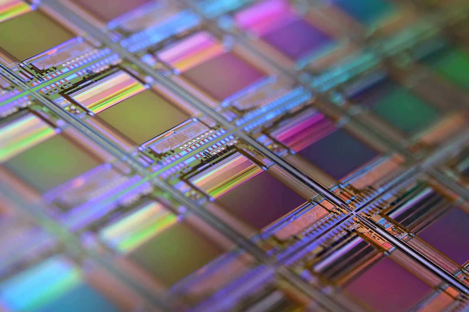 Macro of a silicon wafer: a grid of iridescent processor dies in purple, green and gold under shallow focus
