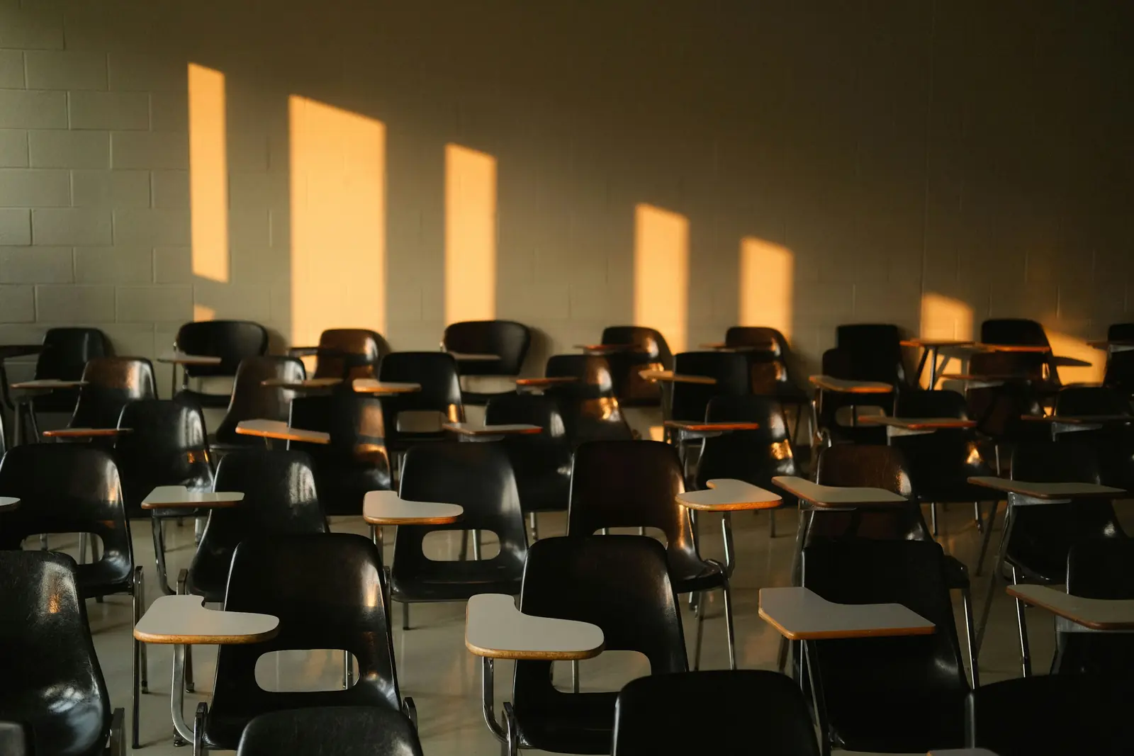 Empty training room with rows of black tablet-arm chairs lit by warm evening sunlight on the wall