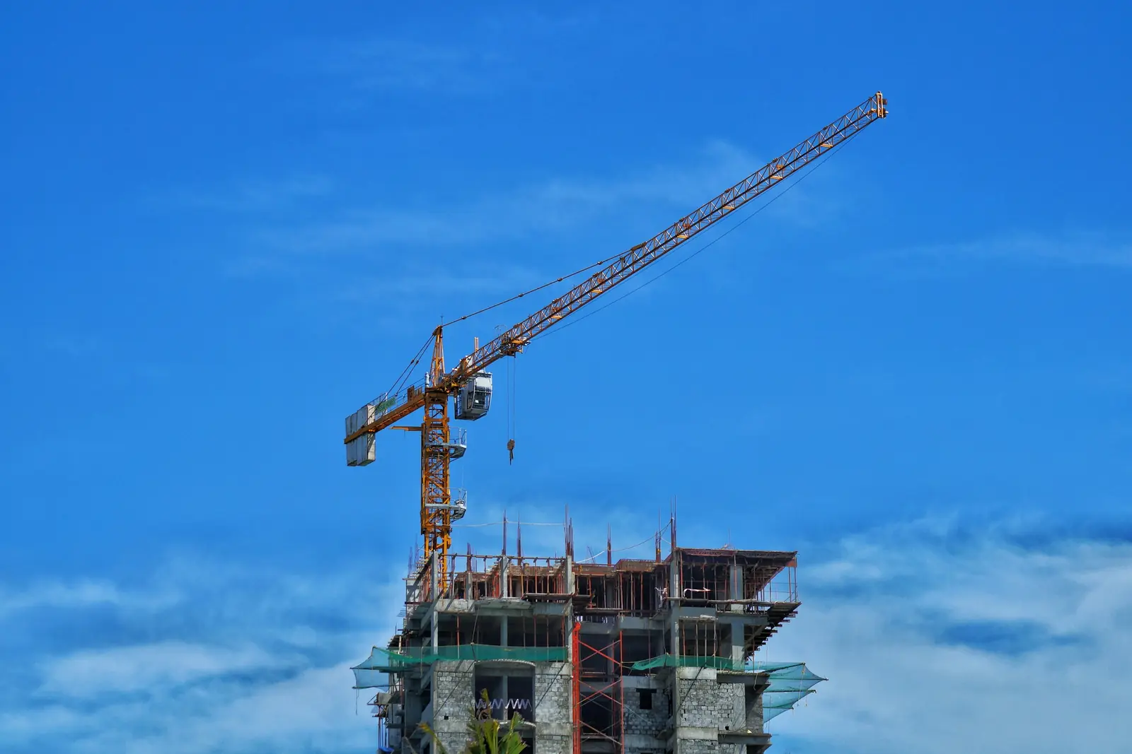 Yellow tower crane above the unfinished concrete floors of a building under construction against a blue sky