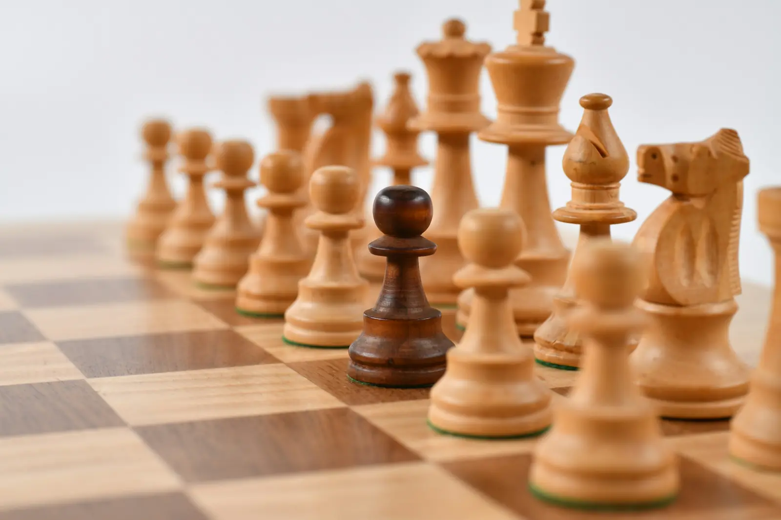 Wooden chess pieces lined up on a board with a single dark pawn standing out among the light pieces