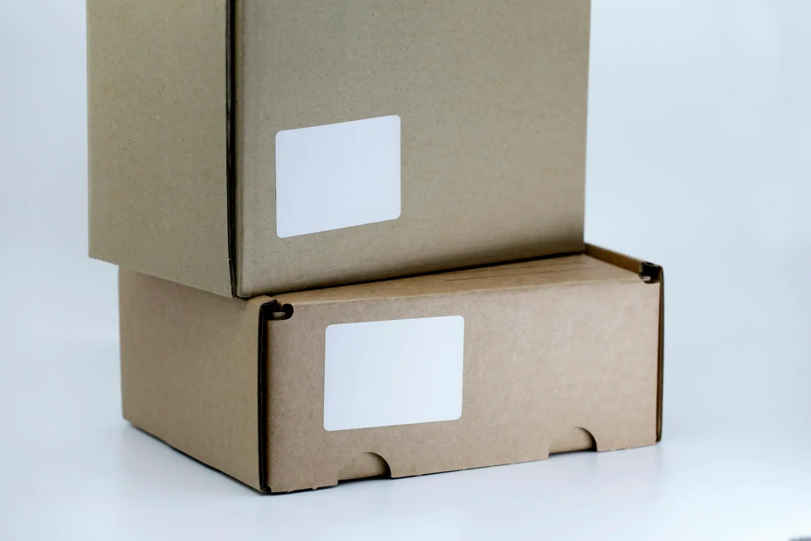 Two stacked cardboard parcels with blank white shipping labels on a plain white surface, ready for pickup