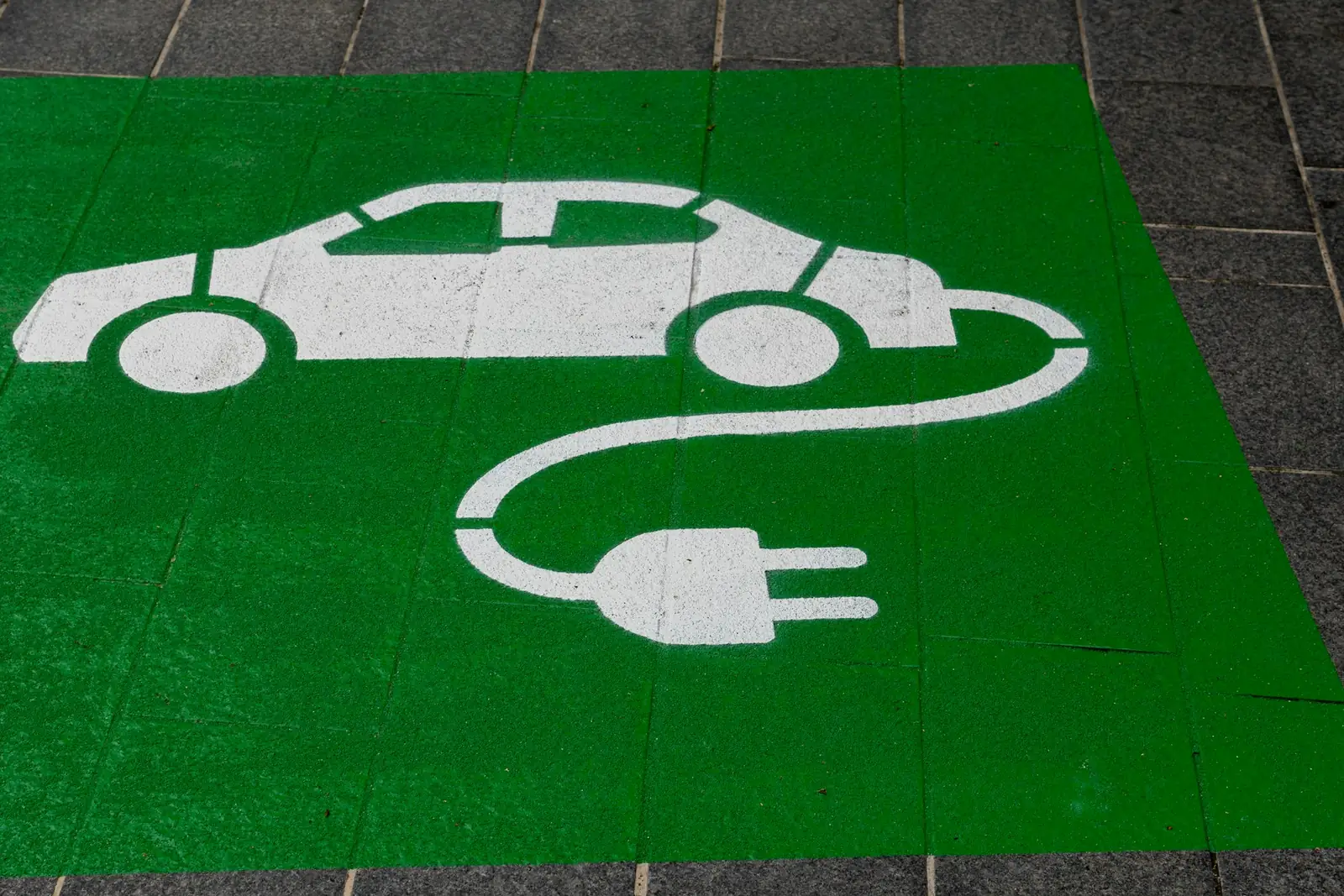 Green electric-vehicle parking bay painted on grey paving, with a white car and charging-plug symbol