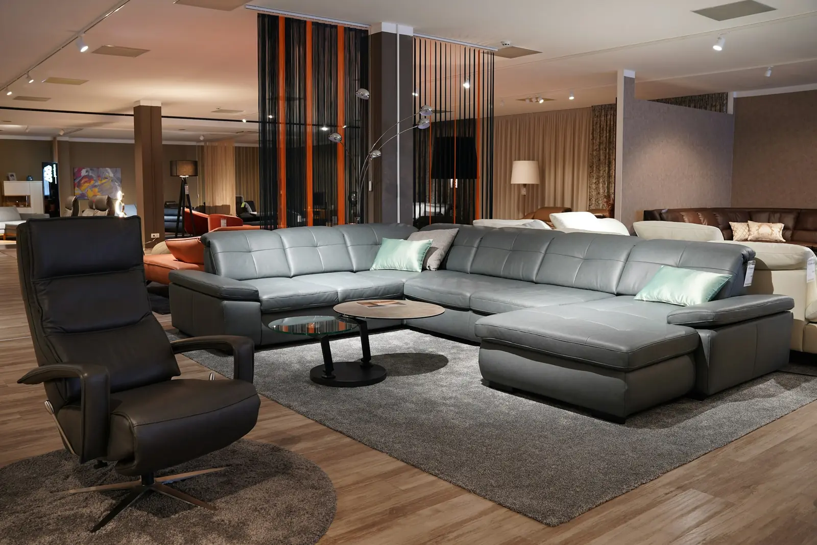 Furniture showroom with a grey sectional sofa, a leather recliner and a round coffee table on a rug