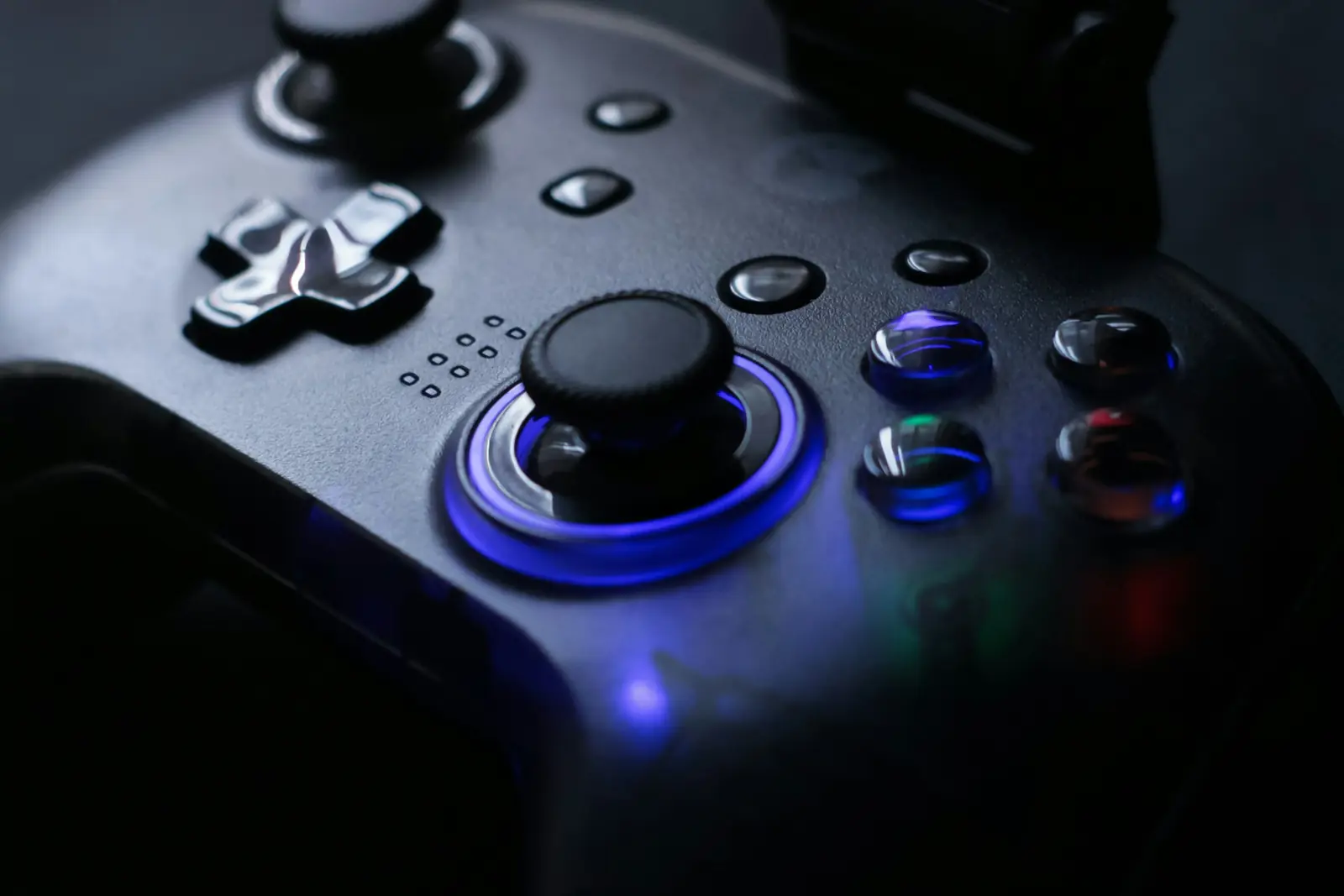 Close-up of a dark game controller with a blue-lit thumbstick ring, glossy face buttons and a directional pad