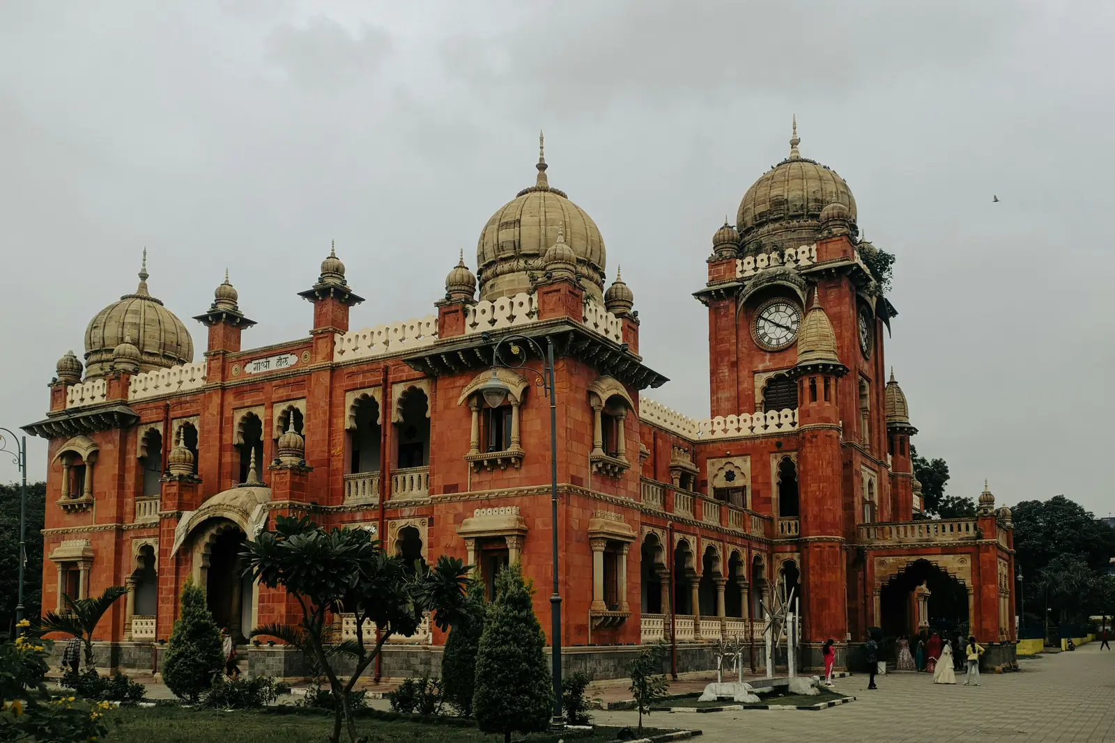 Gandhi Hall in Indore, a red sandstone Indo-Gothic town hall with pale domes and a clock tower, under a monsoon sky