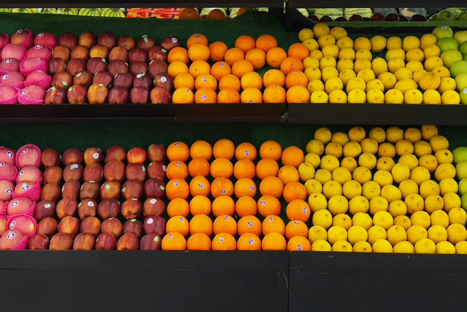 Rows of red apples, oranges and lemons neatly stacked in a supermarket fresh produce section