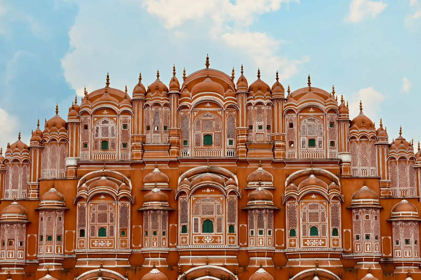 Pink sandstone façade of Hawa Mahal in Jaipur, with tiers of latticed jharokha windows and domes under a cloudy sky