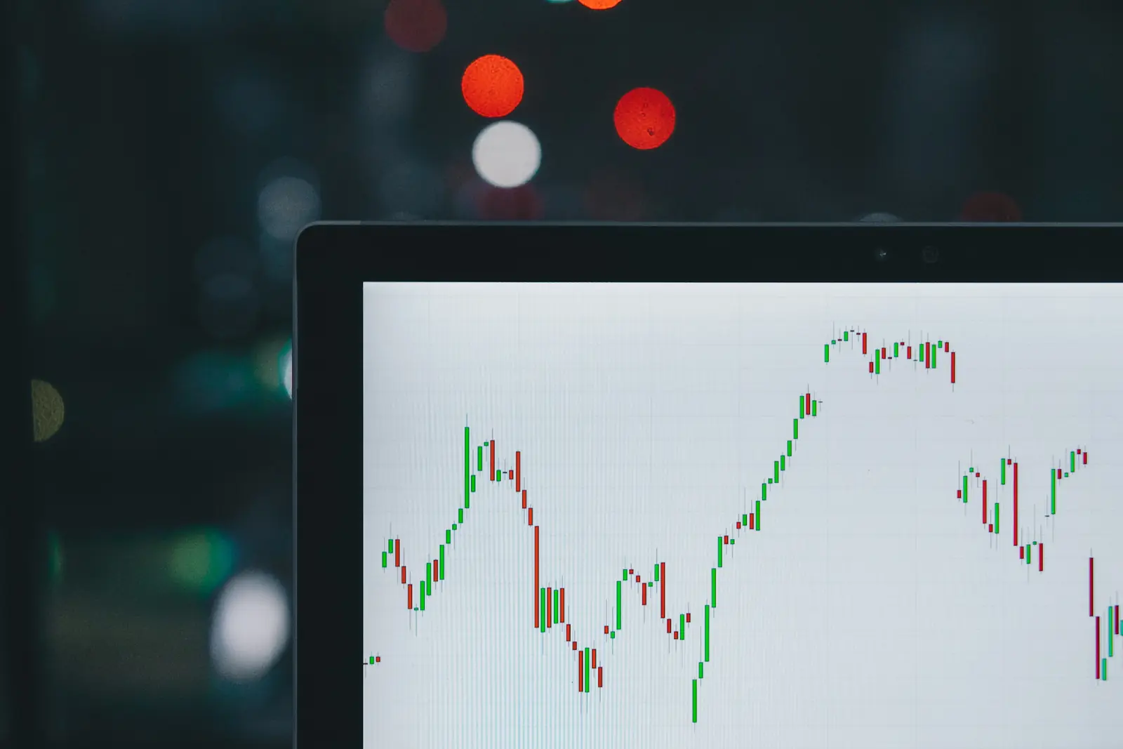 Red and green candlestick stock chart on a laptop screen against blurred city lights at dusk
