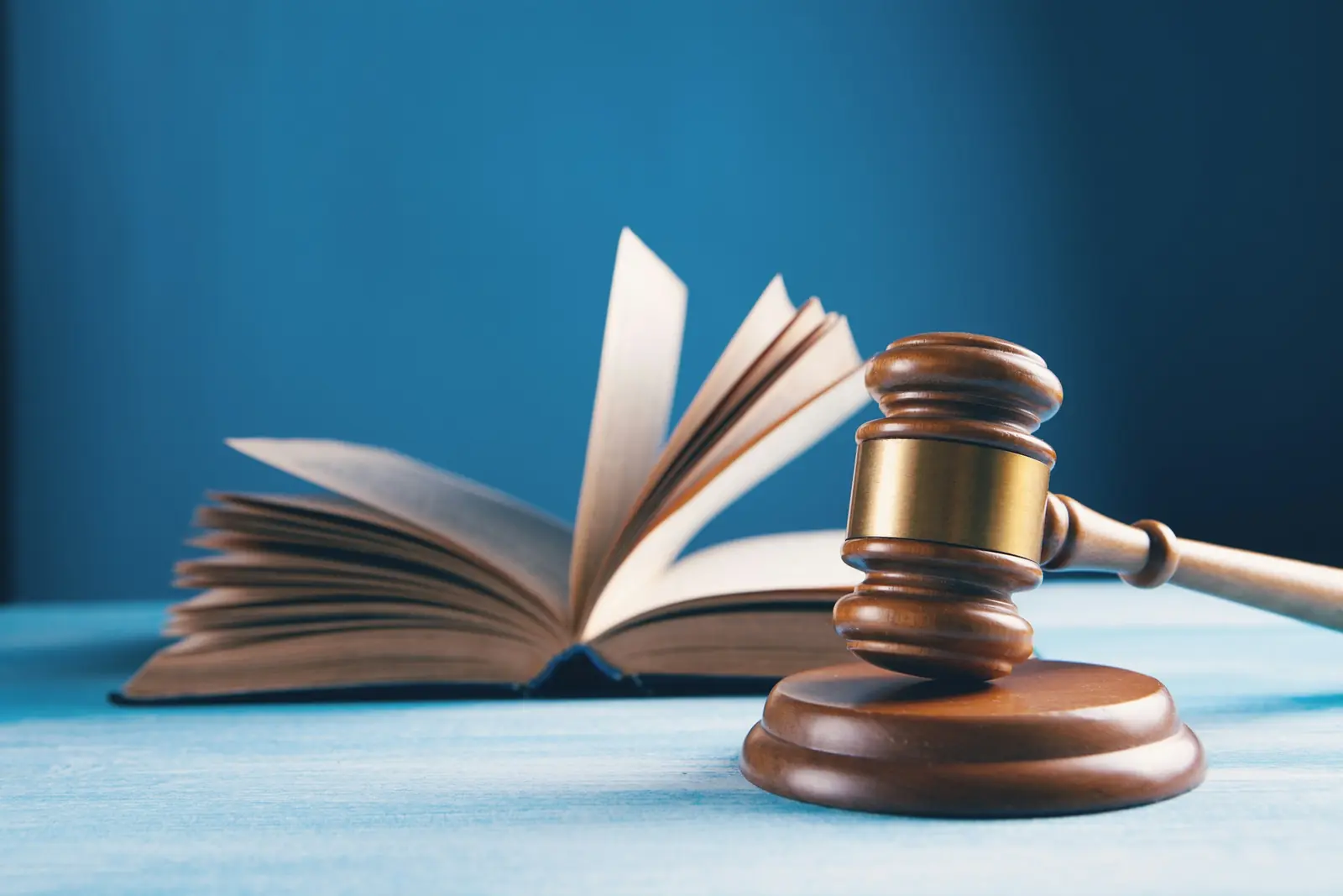 Wooden judge's gavel on its sound block in front of an open book against a deep blue background