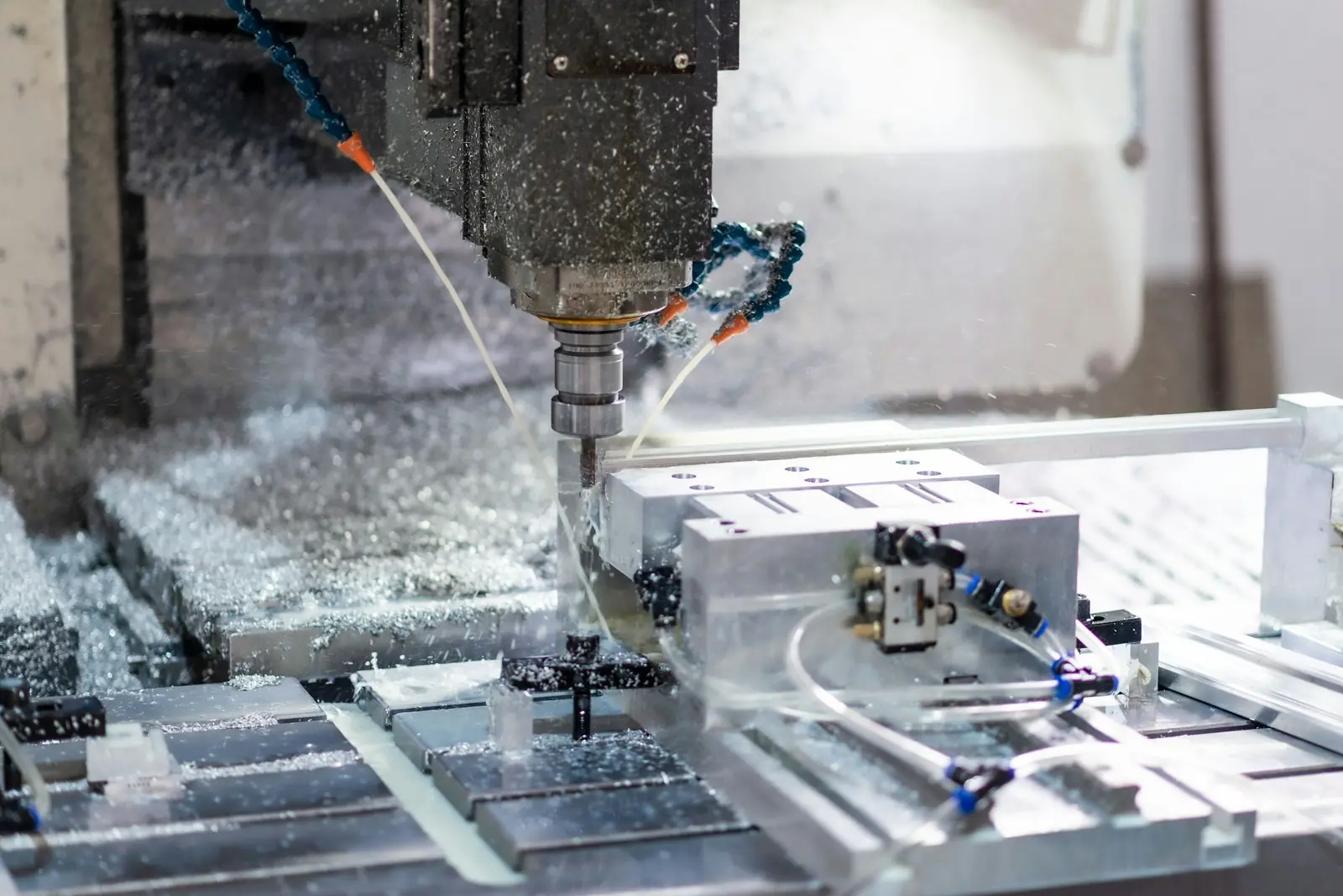 CNC milling machine spindle cutting an aluminium block, with coolant spraying and metal chips on the bed