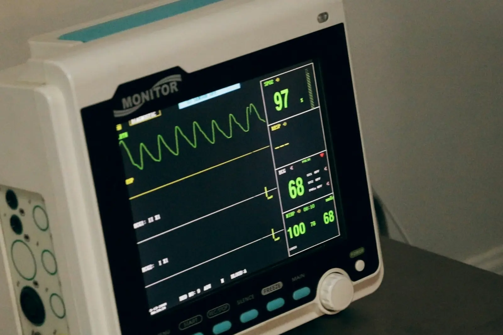 Bedside patient monitor showing oxygen saturation, pulse and blood pressure readings with a green waveform