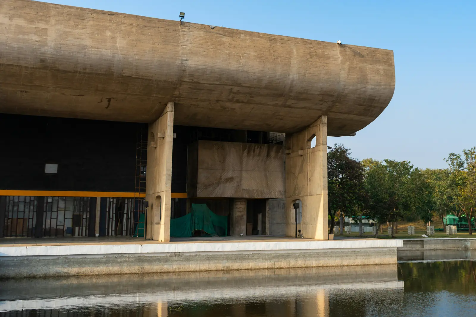 Curved concrete portico of the Palace of Assembly in Chandigarh Capitol Complex, reflected in its pool under a blue sky