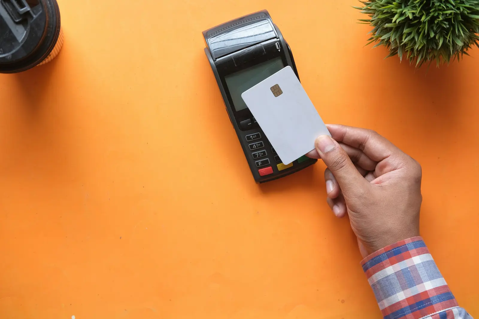 Hand holding a plain white chip card to a card payment terminal on a bright orange table, seen from above