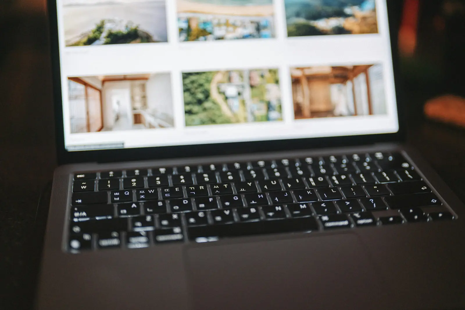 Laptop screen showing a grid of property listing photos of homes and interiors above a backlit keyboard