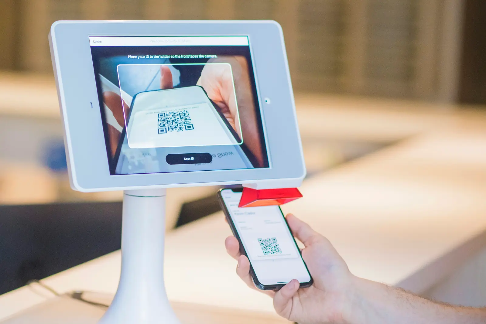 Self check-in tablet on a stand at a reception counter, scanning a QR code pass held up on a visitor's phone