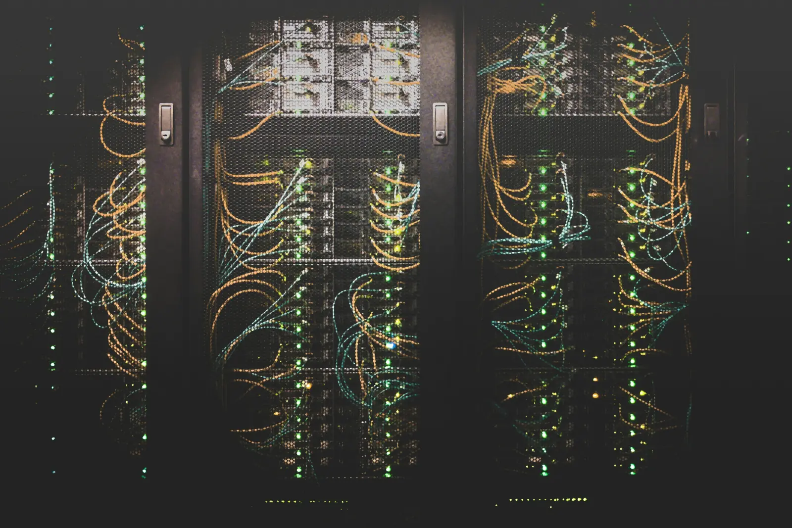 Data centre server racks behind mesh doors, threaded with orange and blue fibre cables and green status lights