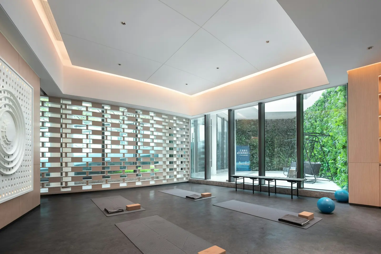 Calm yoga studio with mats, blocks and exercise balls laid out on a grey floor beside a wall of plants
