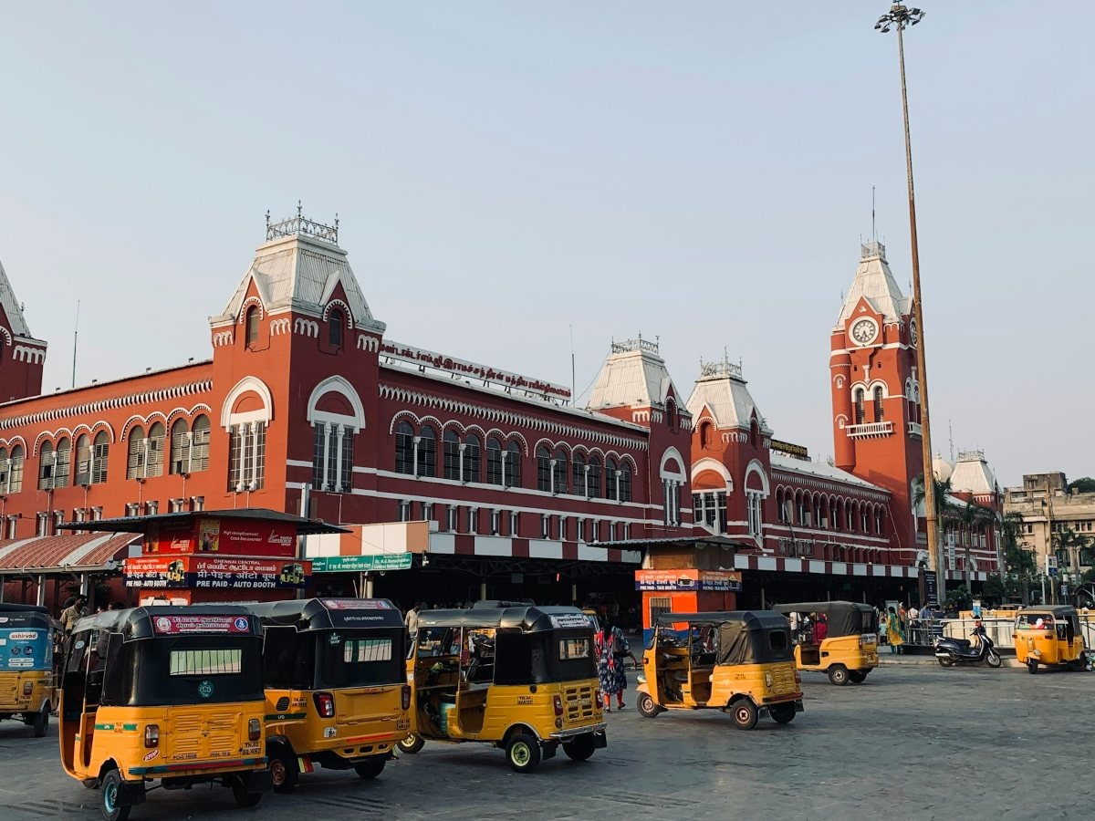Red Gothic-style Chennai Central railway station and its clock tower, with yellow auto-rickshaws in front