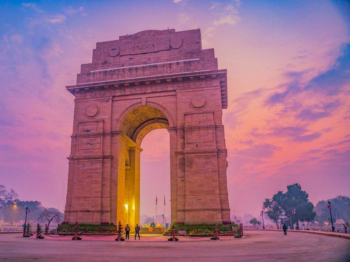 India Gate war memorial on Kartavya Path, New Delhi, lit at its base under a pink twilight sky
