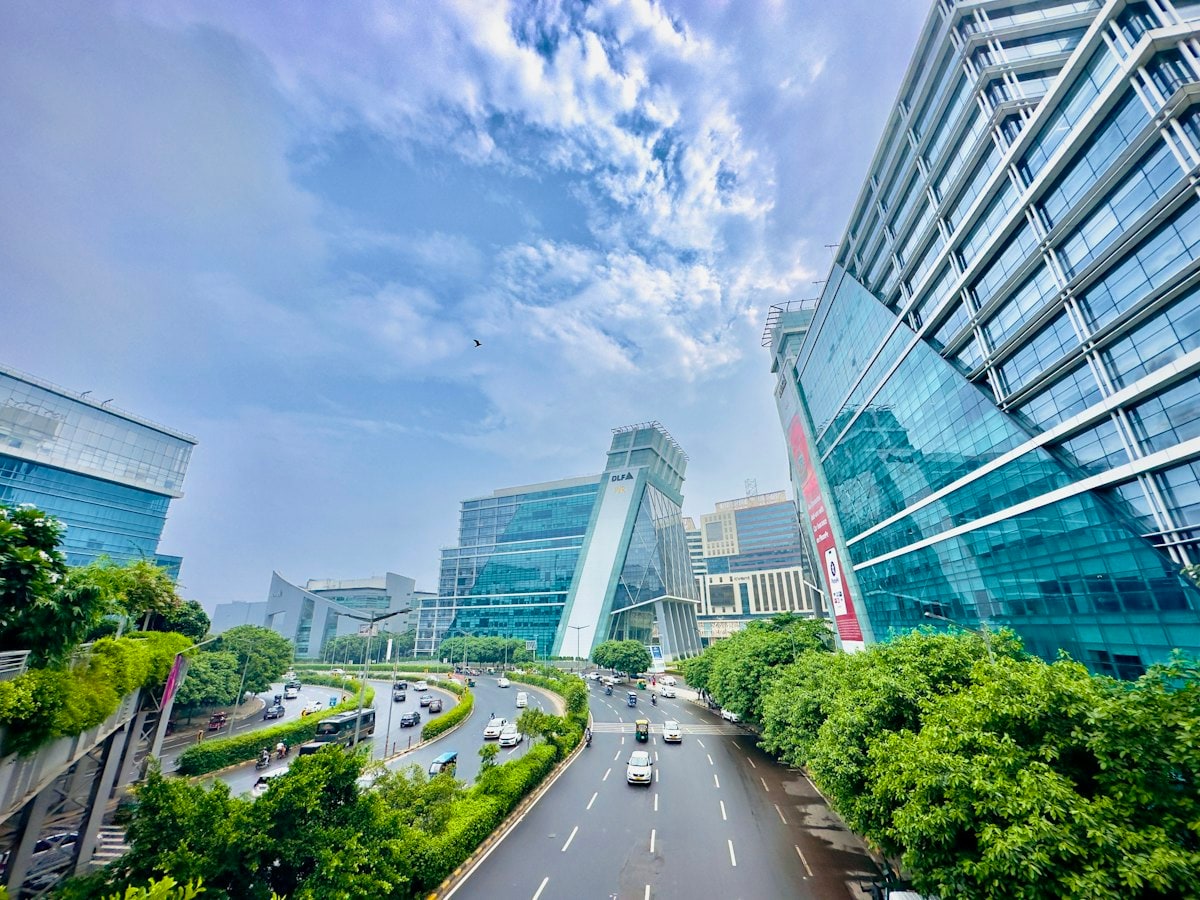 Glass office towers of DLF Cyber City beside a tree-lined road in Gurugram, Haryana, on a bright day