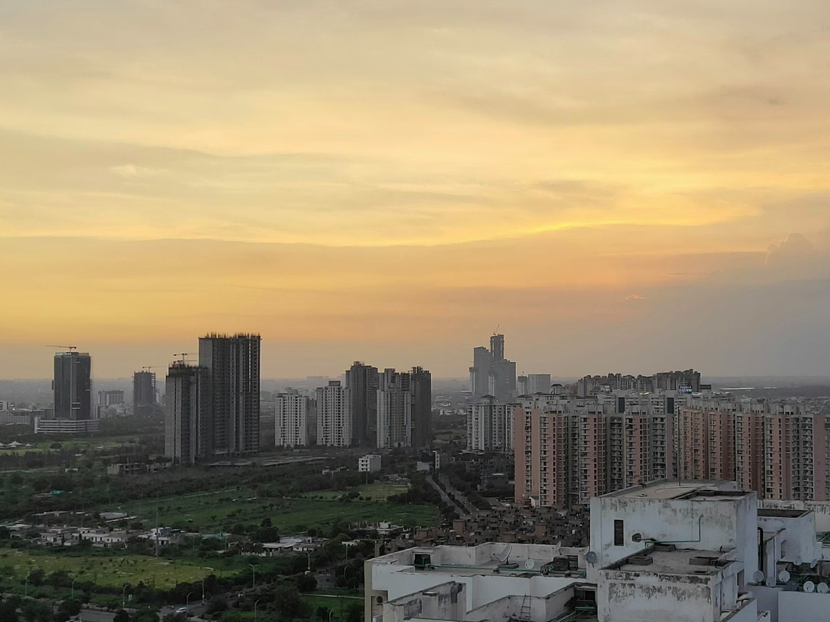 High-rise residential towers on the Noida skyline under a golden sunset sky, seen from a rooftop