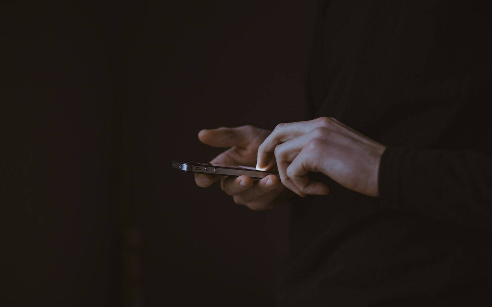 Hands typing a chat message on a smartphone in a dark room, lit only by the screen glow