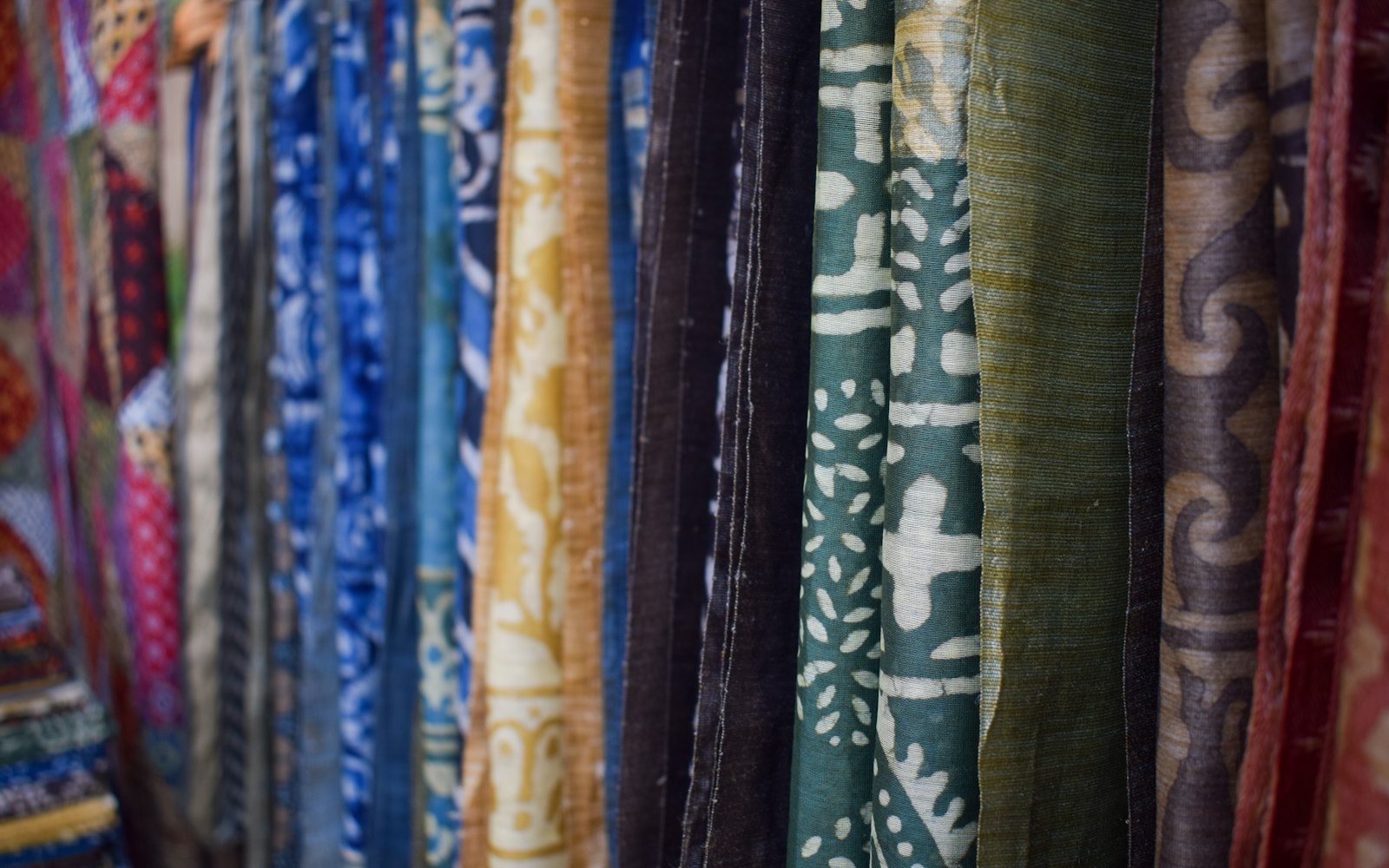 Colourful patterned fabrics in indigo, mustard and green hanging side by side in a textile boutique