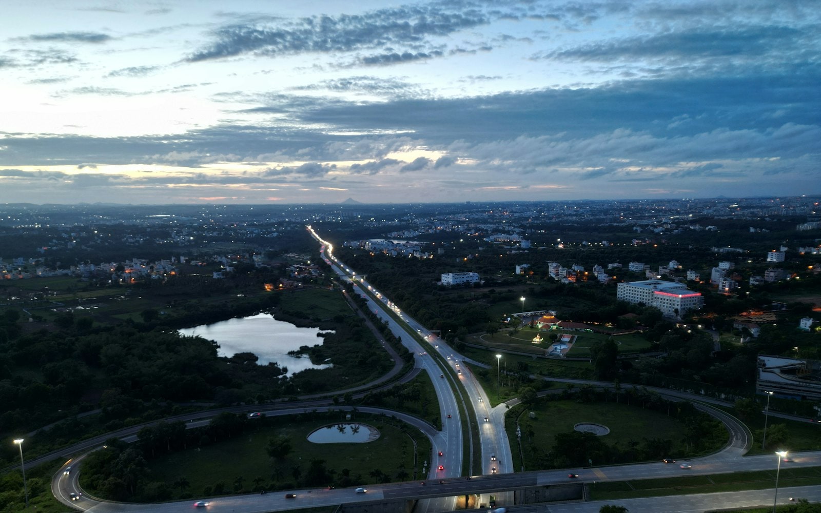 Aerial view of a highway interchange at dusk, with vehicle headlights streaming towards the city